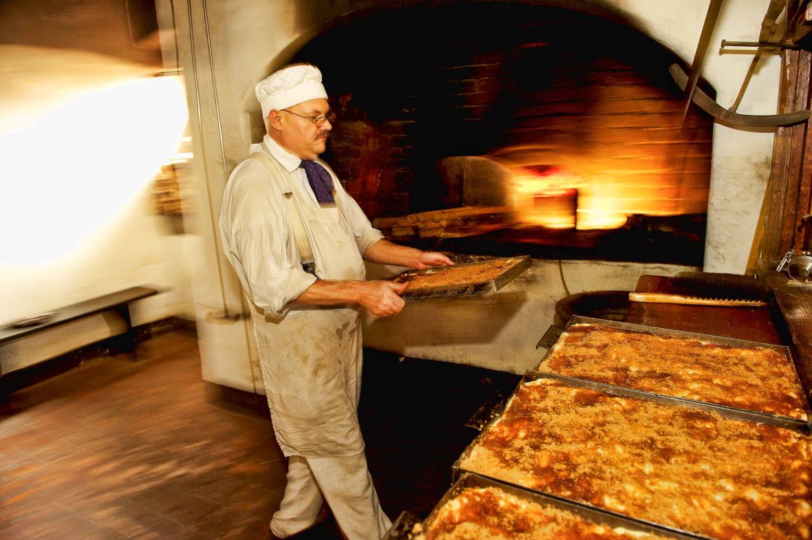 A man moves trays of baked goods from the oven.